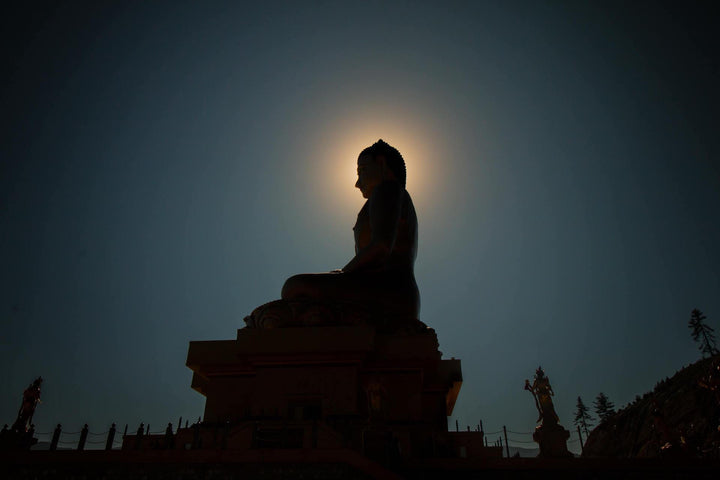 Buddha statue silhouette meditating with sun aura and CBD