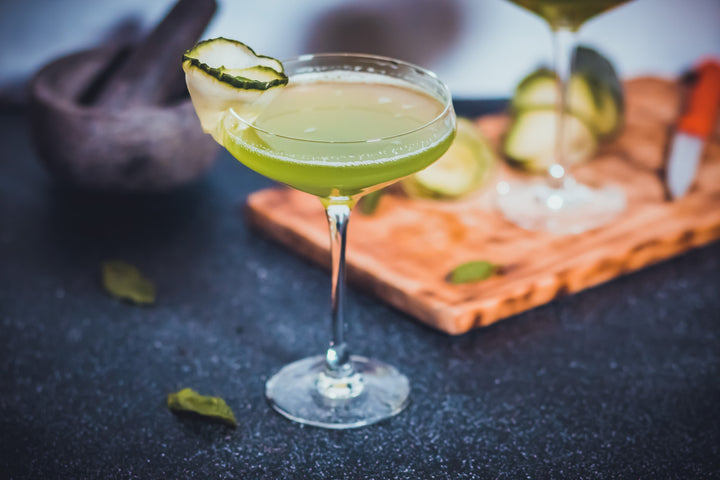 CBD cocktail with green coloring and lime garnish artfully placed next a cutting board with lime and a martini glass